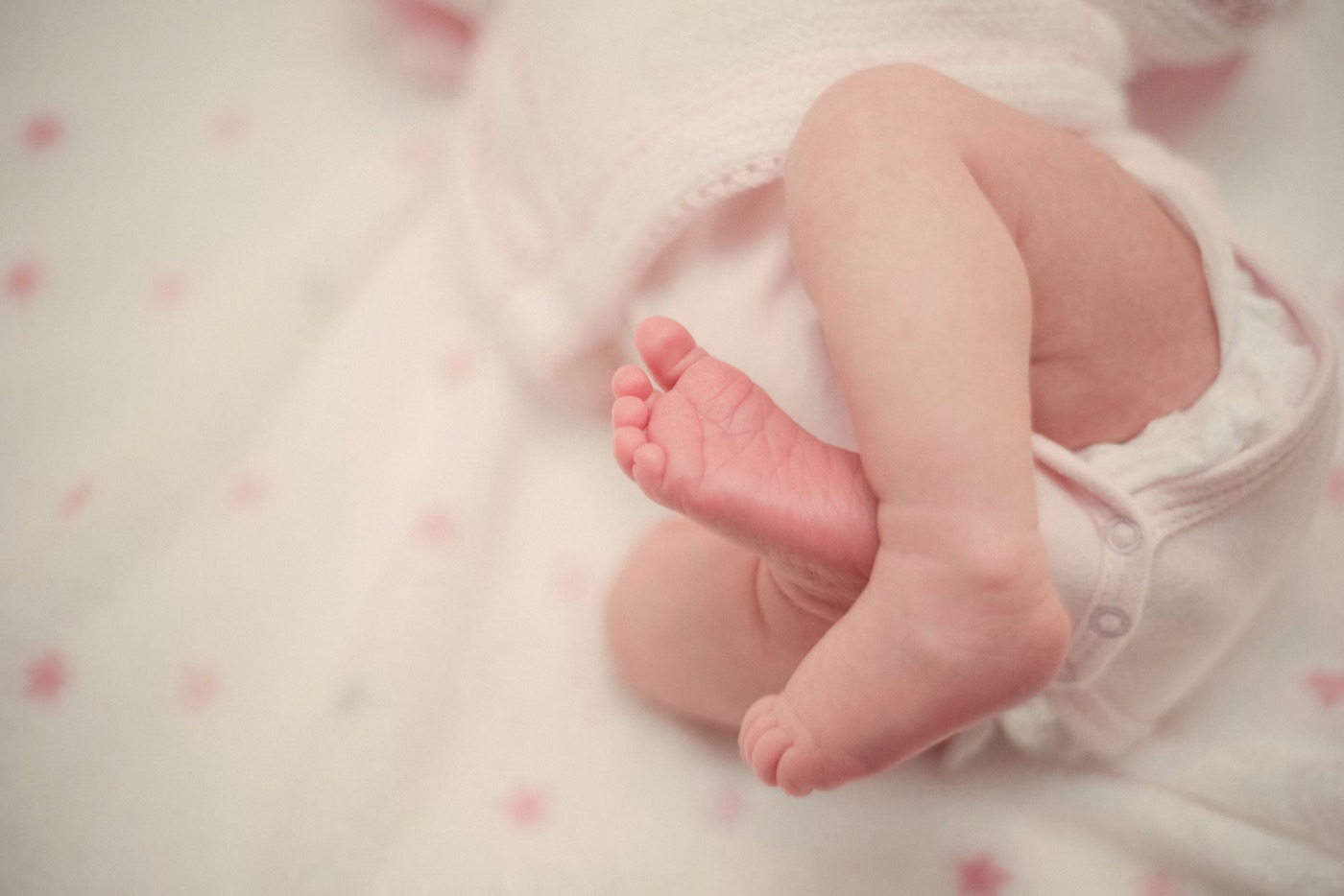 A newborn baby’s bare feet, gently curled, resting on a soft pink blanket.